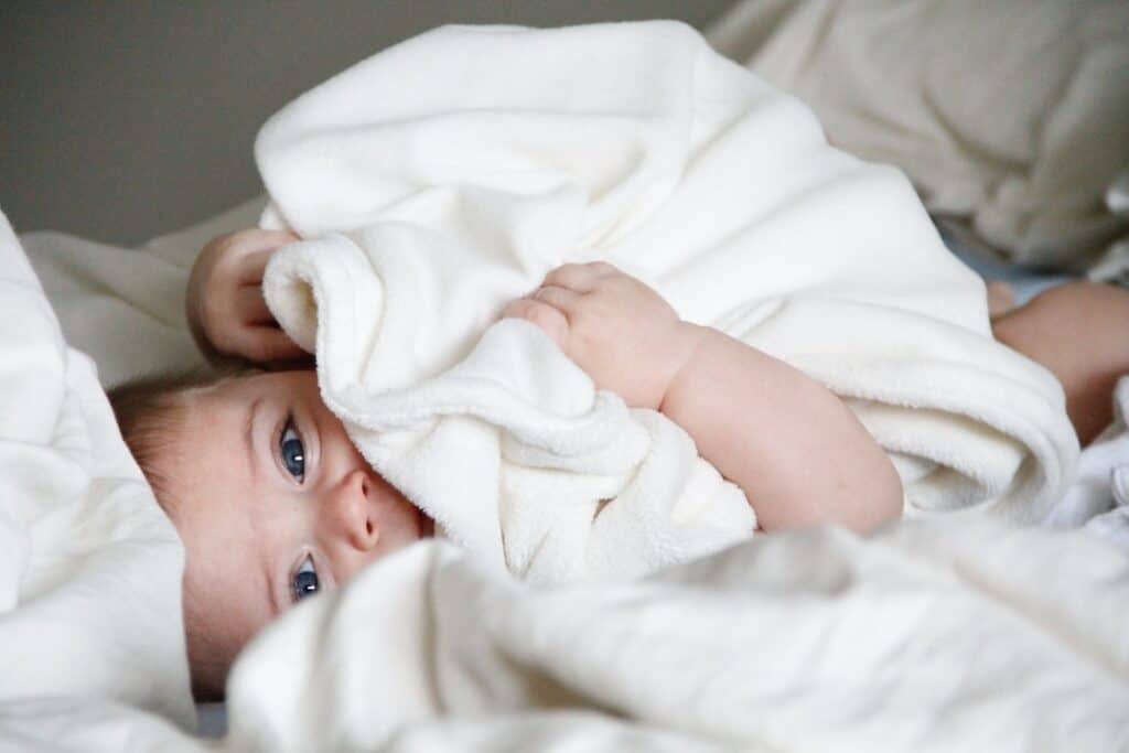 A baby is hiding under a blanket in a bed.