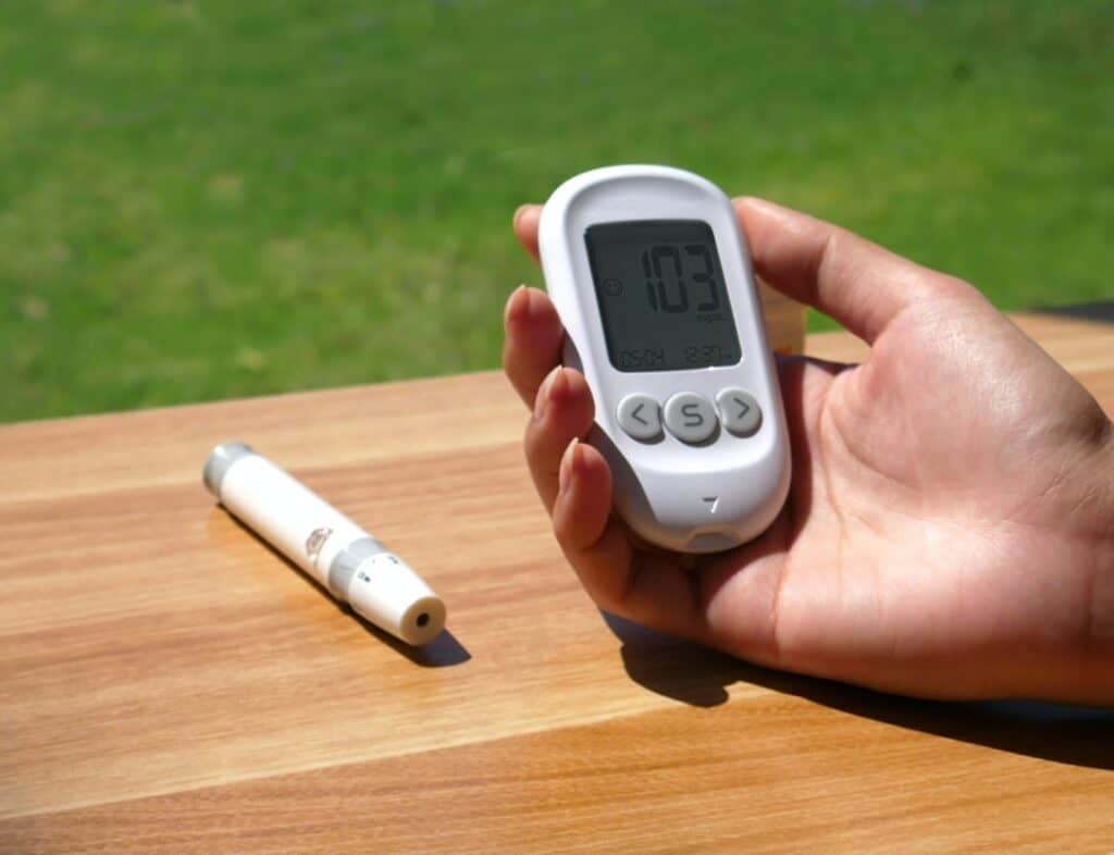A person holding a blood glucose meter on a wooden table.