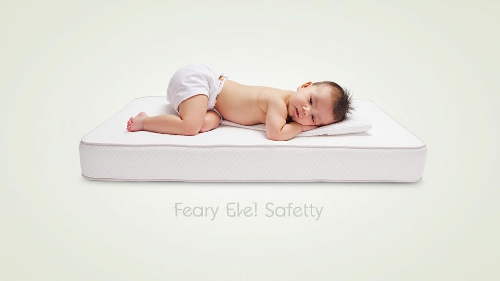 A baby in a diaper lies on its side on a mattress with a small pillow; the words "Feary Ele! Safetty" appear below.